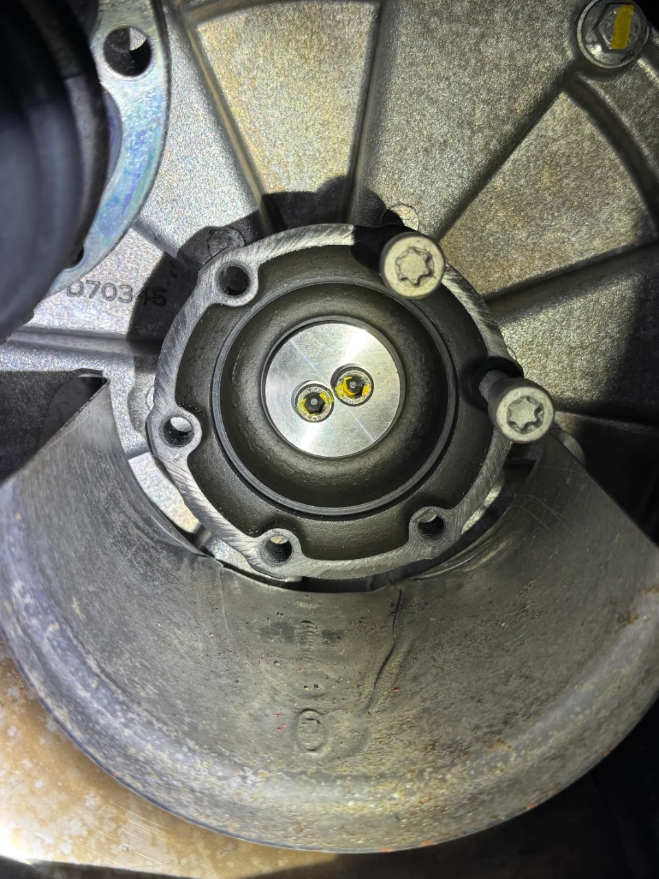 A close-up view of a car's drivetrain component, possibly a differential or transmission output, with visible bolts and metal housing.