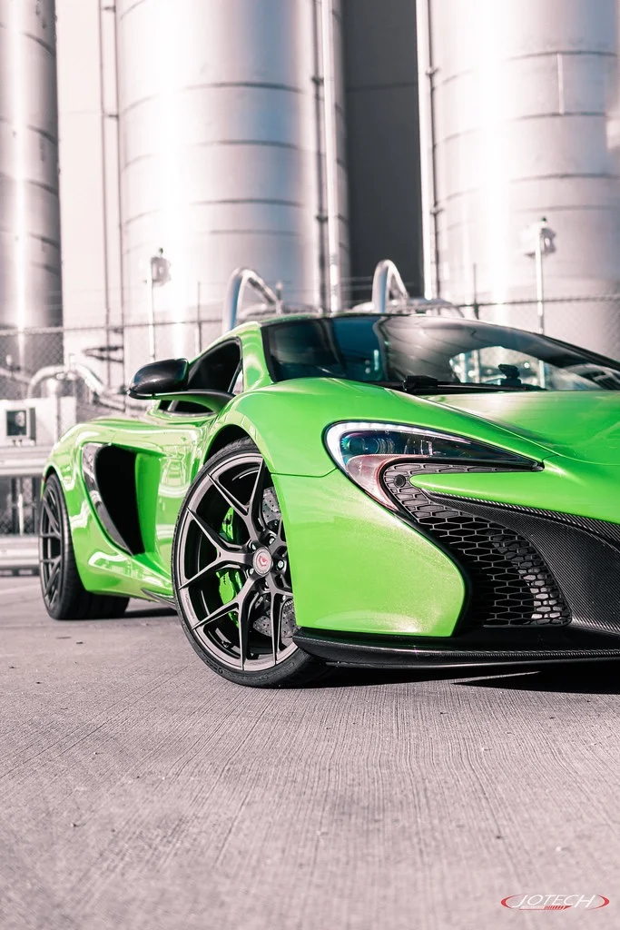 Bright green McLaren supercar with Vossen wheels and carbon fiber aero parked in front of industrial silos.