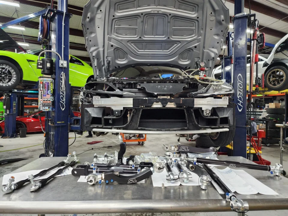 Nissan GT-R on a lift in a Jotech Motorsports shop with new suspension and chassis components laid out on a table.