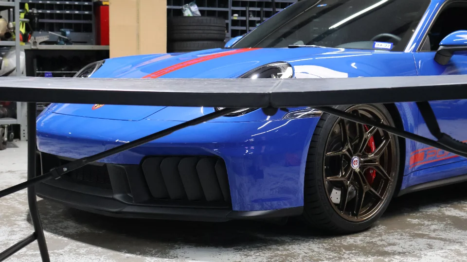A blue Porsche 911 GT3 with HRE wheels and red brake calipers parked in a performance shop.
