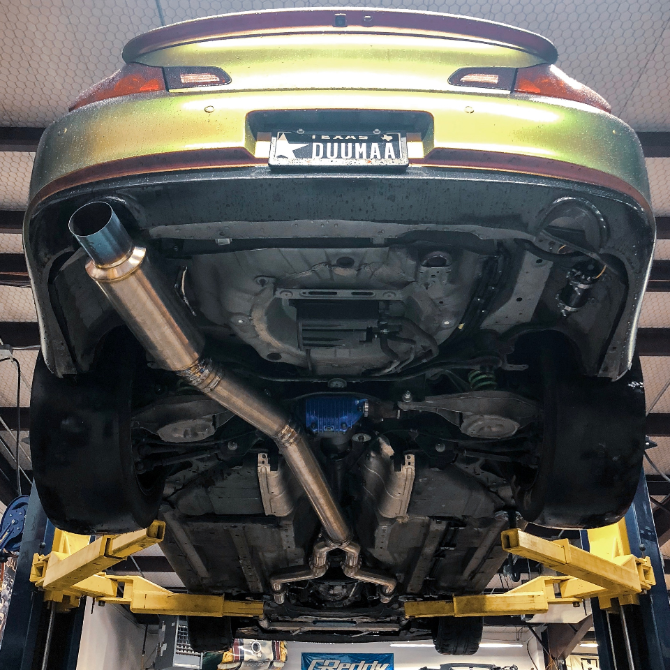 Underside view of a custom exhaust system and differential on a car lifted in a performance shop.