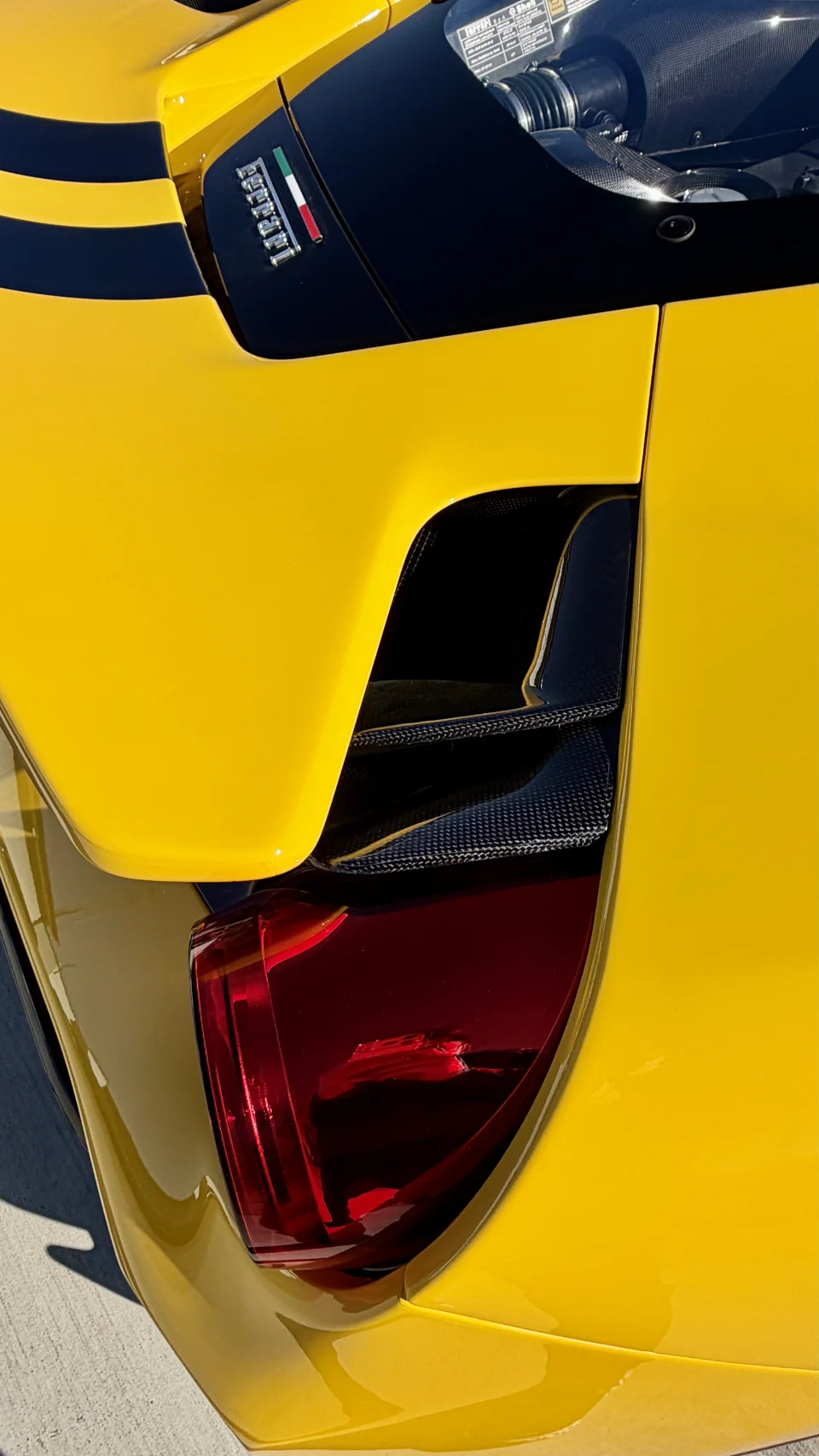 Close-up detail of the rear of a yellow Ferrari supercar, showing carbon fiber vents, taillight, and engine cover.