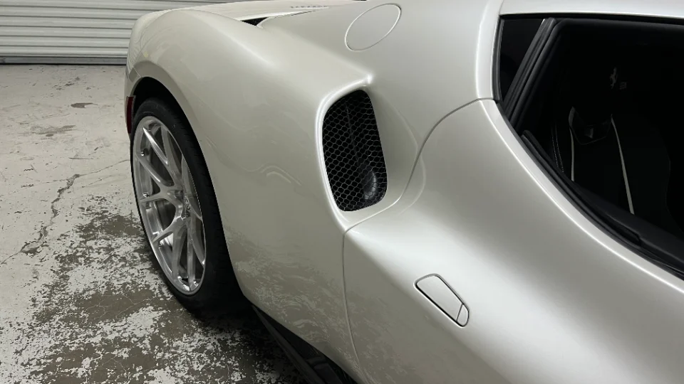 Close-up of a white Ferrari sports car's rear wheel and side air intake, showcasing custom wheels in a garage setting.
