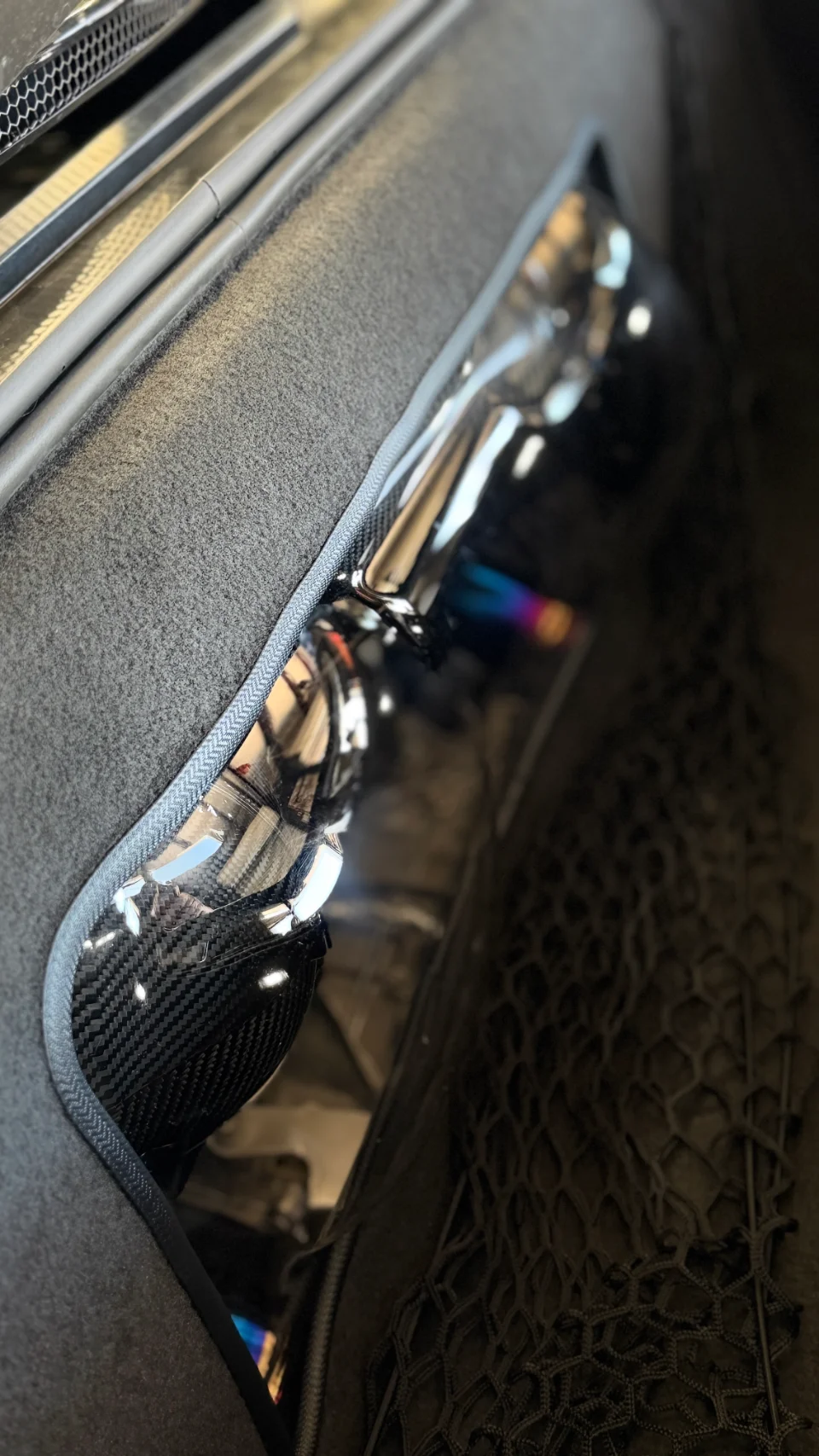 Close-up detail of a carbon fiber performance intake system visible through a clear panel in a car's interior or trunk area.