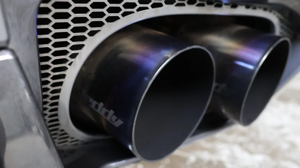 Close-up of Greddy titanium exhaust tips on a performance car, showcasing the burnt titanium finish.