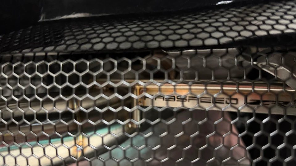 Close-up detail of a polished metal performance pipe with 'ABS SPEED' branding visible behind a hexagonal mesh grille.