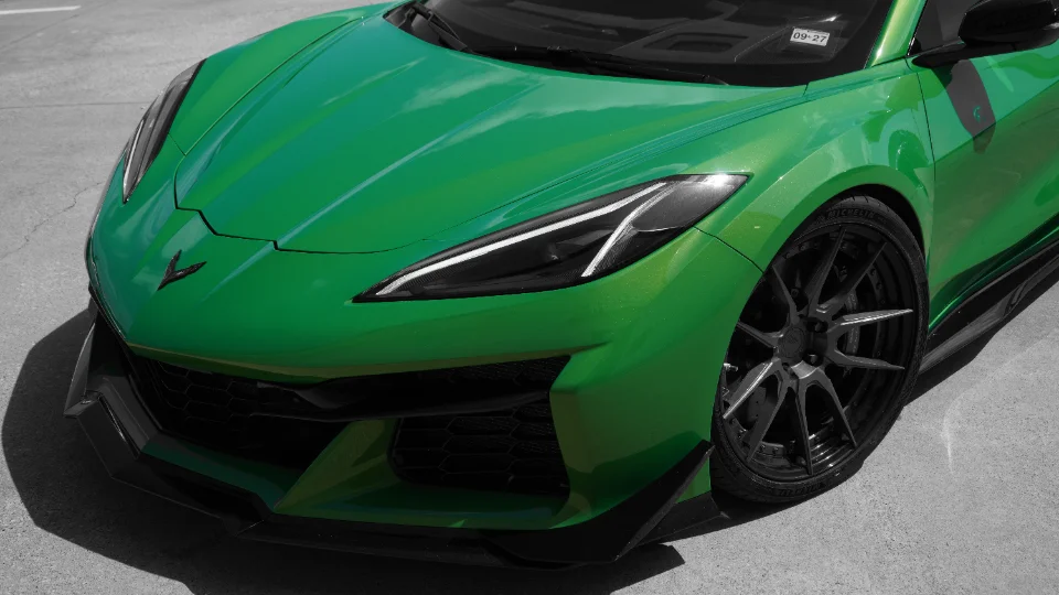 A close-up of a vibrant green Chevrolet Corvette C8 Z06 with custom black multi-spoke wheels and an aggressive front splitter.