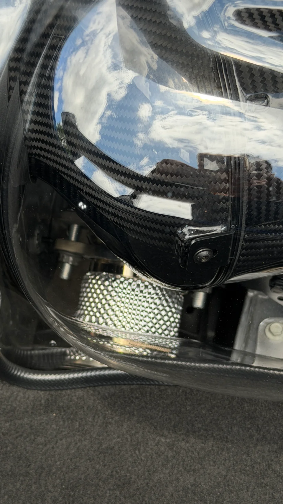 Close-up of a carbon fiber air intake system with a clear cover, reflecting the sky and clouds.
