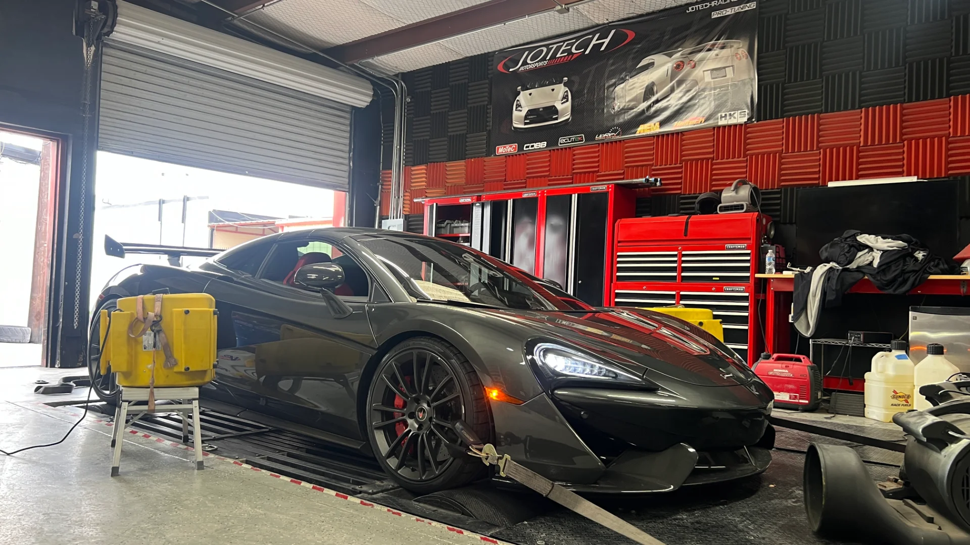 A grey McLaren 570S strapped to a dynamometer at Jotech Motorsports for performance tuning.