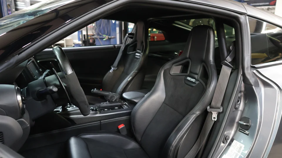 Interior view of a Nissan GT-R featuring Recaro seats, a carbon fiber steering wheel, and center console.
