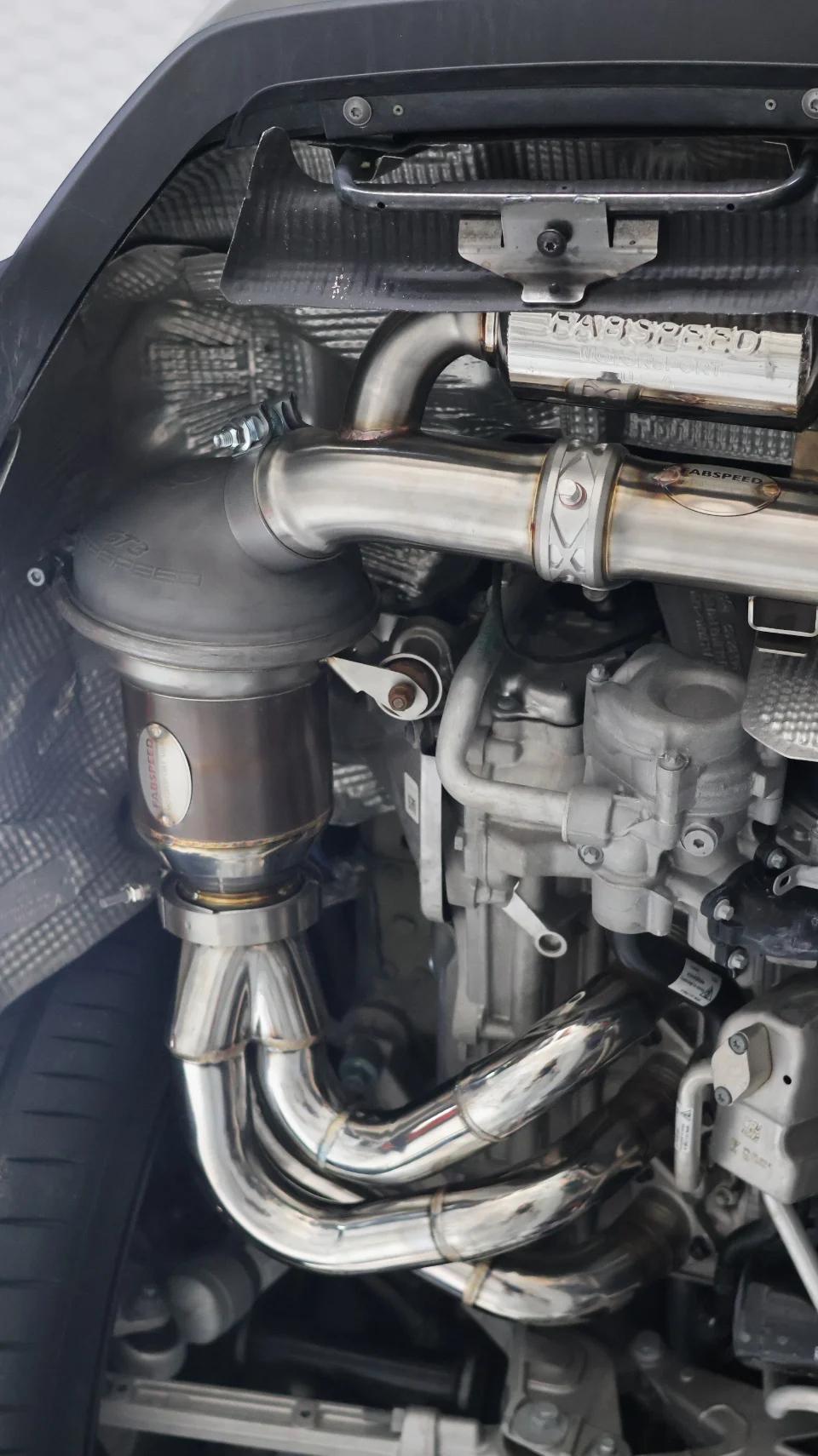 Close-up of a Fabspeed stainless steel exhaust system with headers and downpipe installed on a car.