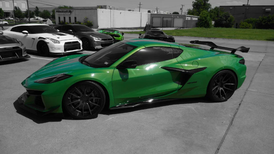 A vibrant green Corvette C8 with aftermarket wheels and carbon fiber aero parked alongside several Nissan GT-Rs.