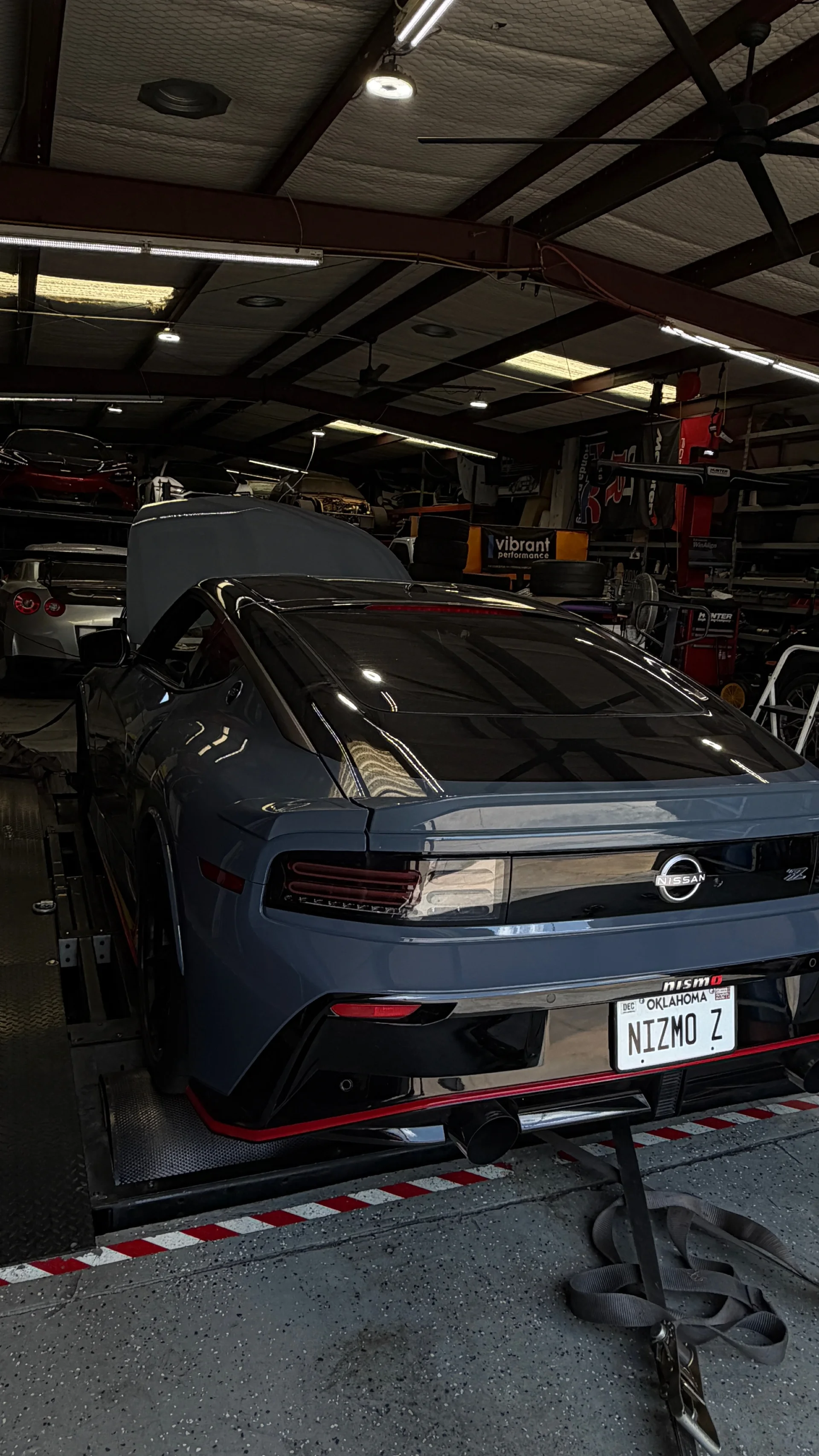 Rear view of a gray Nissan Z Nismo strapped down on a dynamometer in a performance tuning shop.