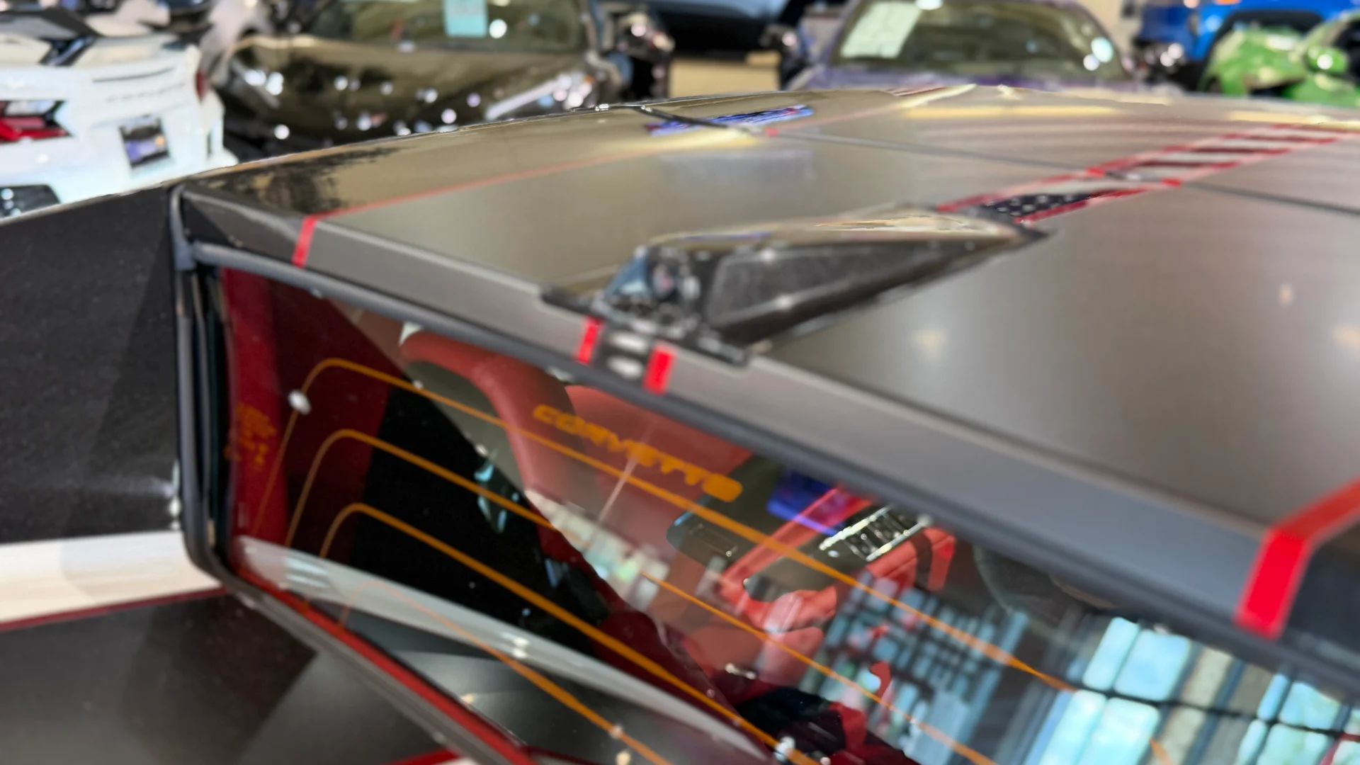 Close-up of a Corvette's rear window and roof with an American flag graphic, reflecting a car dealership interior.