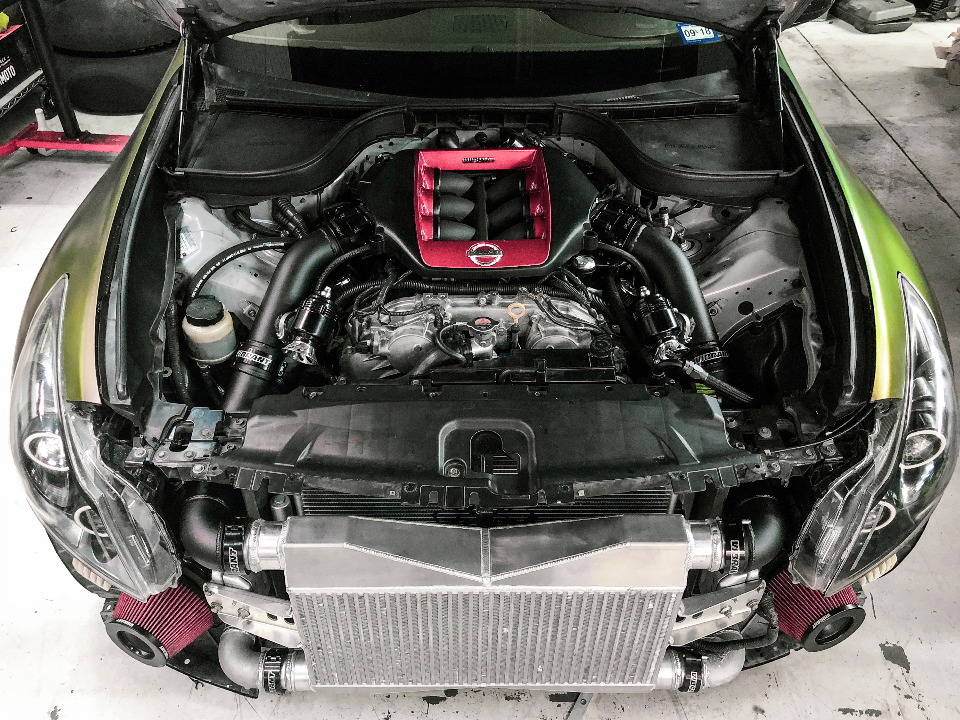 Overhead view of a modified Nissan GT-R VR38 engine bay with a large front-mounted intercooler, aftermarket intake manifold, and air filters.