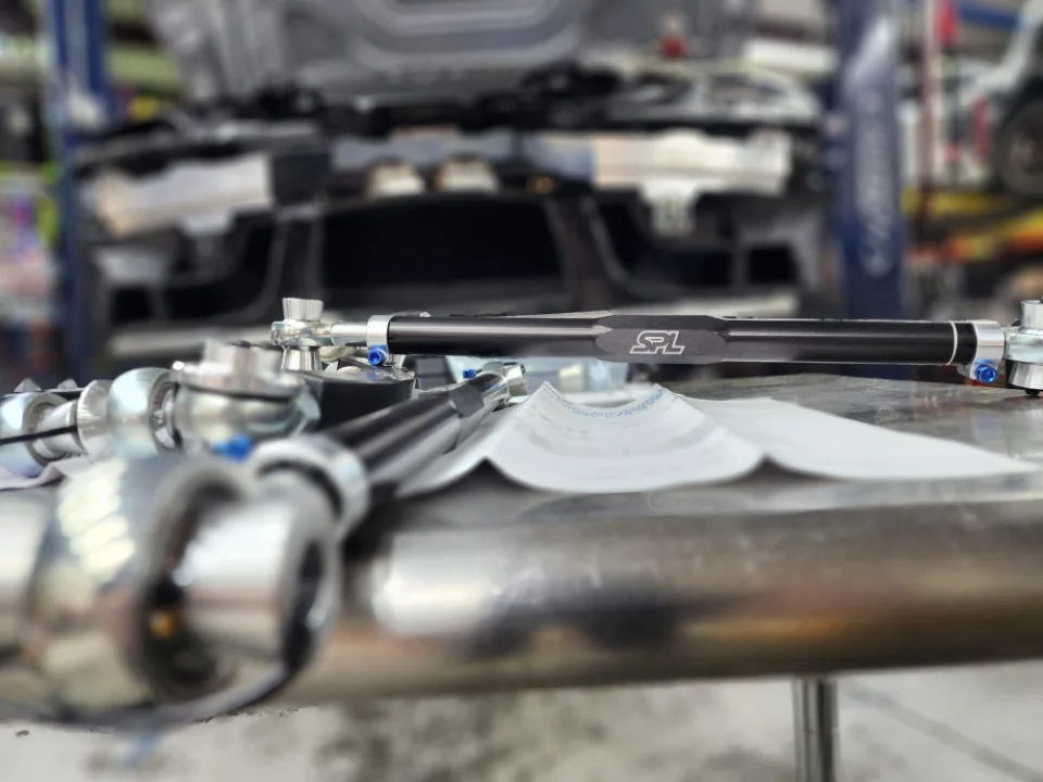 SPL Parts suspension components, including control arms, laid out on a table in a performance tuning shop.