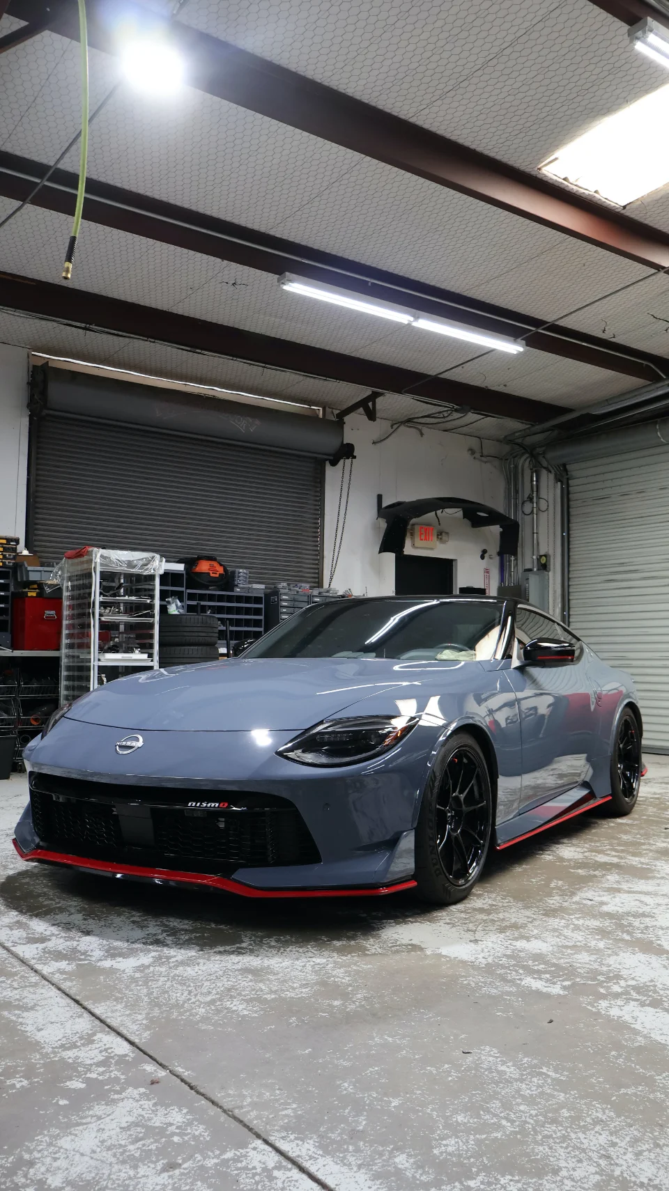 A gray Nissan Z Nismo with red accents and black wheels parked inside a performance tuning shop.