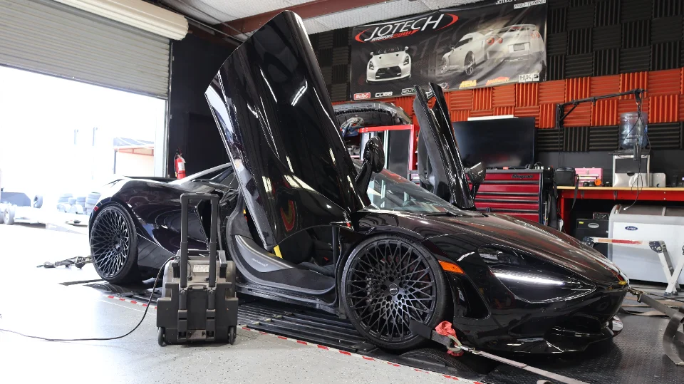 Black McLaren 720S with butterfly doors open, strapped to a dynamometer at Jotech Motorsports for performance tuning.