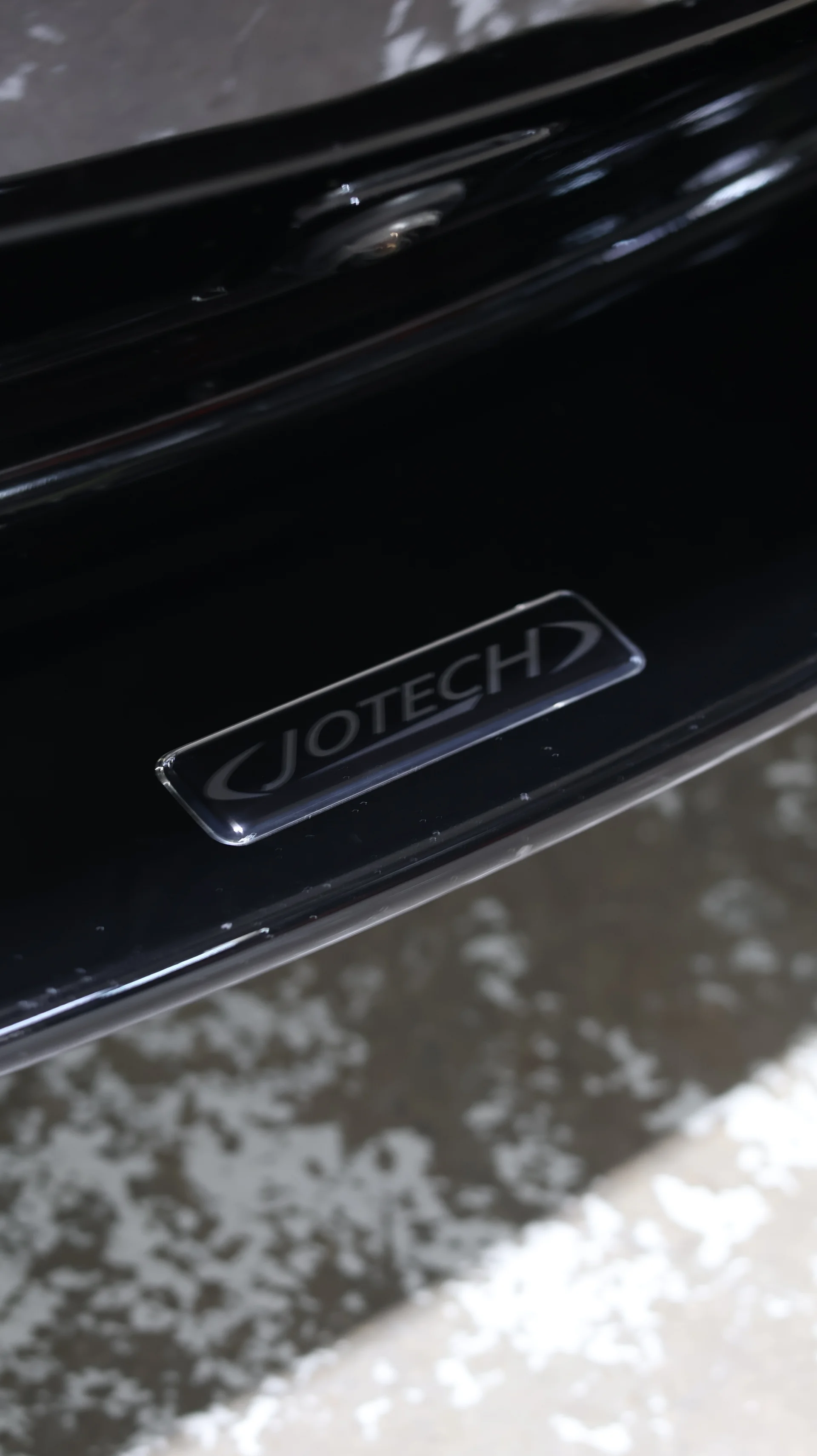 Close-up of a Jotech logo emblem on a black car surface, possibly a door sill or body panel.