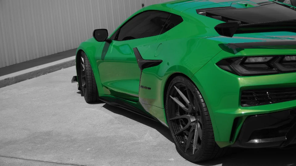 Green C8 Corvette with custom black wheels and a rear spoiler parked outdoors, showcasing its sleek design.