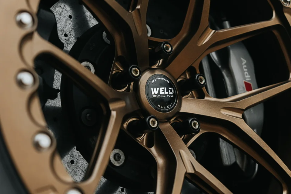 Close-up of a bronze Weld Racing forged wheel with Audi brake caliper and drilled rotor.