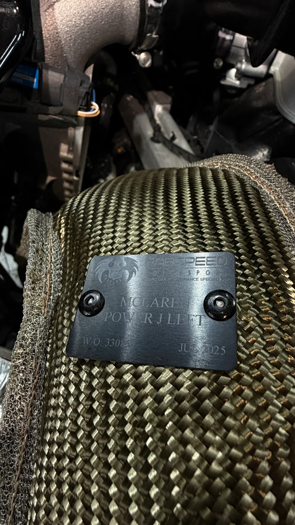 Close-up of a Peer Speed heat shield on a McLaren performance exhaust component in an engine bay.