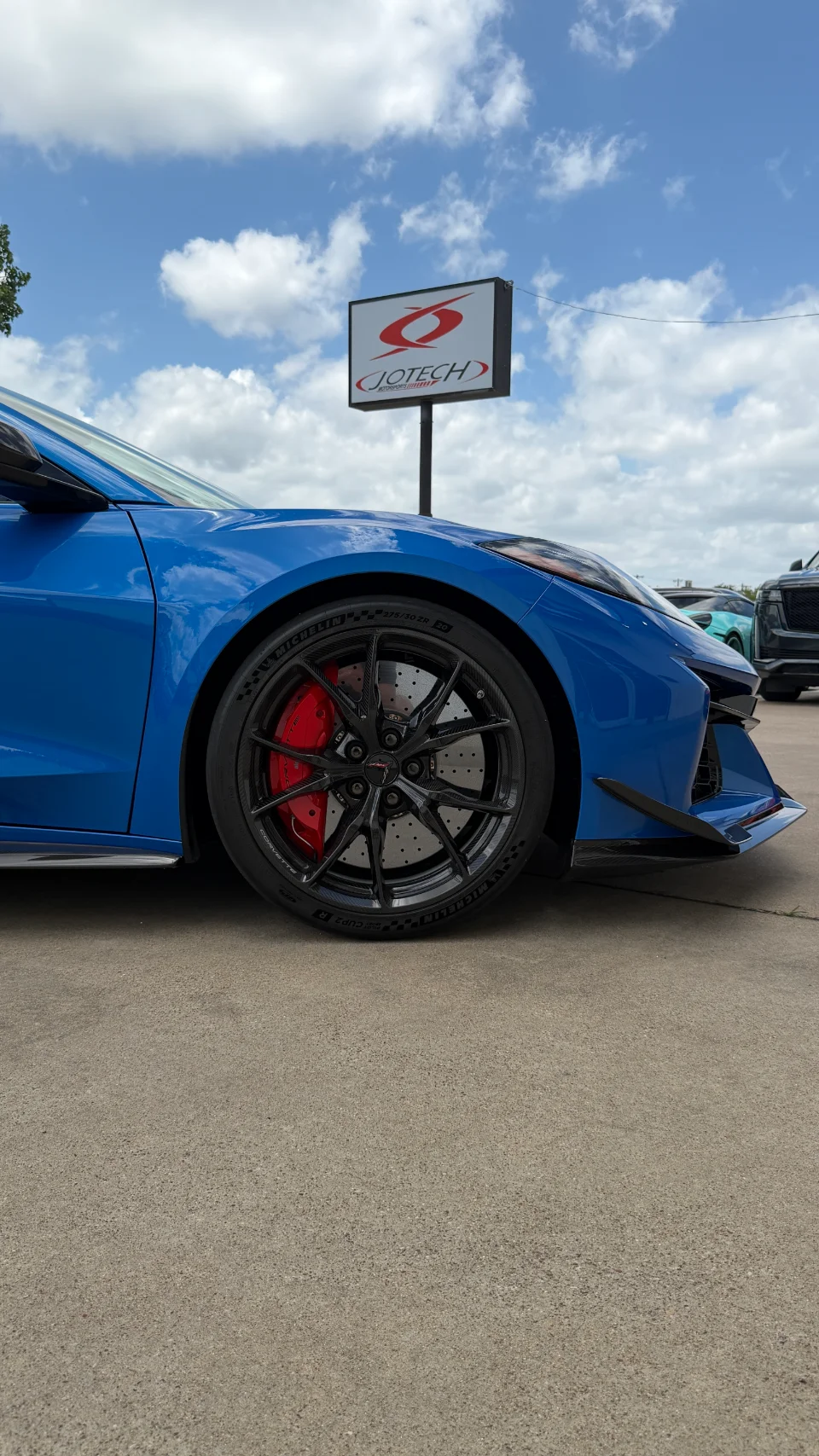 A blue Corvette Z06 with red brake calipers and black carbon wheels parked outside Jotech Motorsports.
