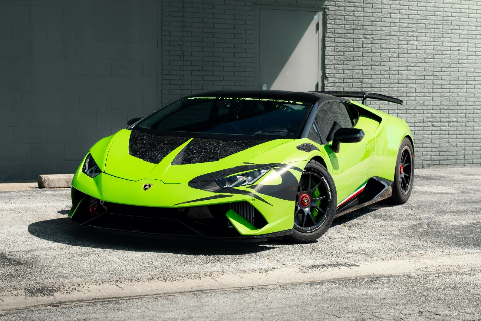 A bright green Lamborghini Huracan with carbon fiber accents and a rear wing parked in front of a brick wall.
