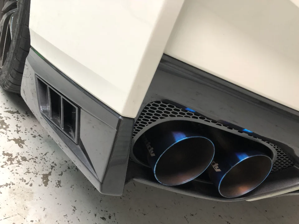 Close-up of a white car's rear bumper featuring aftermarket blue titanium exhaust tips and a black diffuser.
