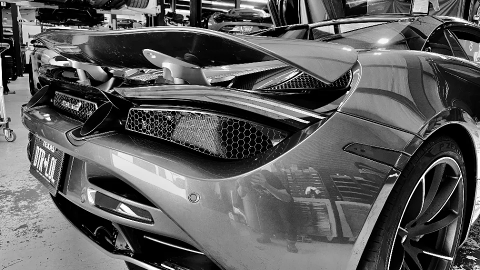 Rear view of a high-performance car, possibly a McLaren, with its active aero wing deployed, inside a Jotech Motorsports shop.