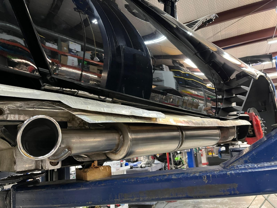 A black car on a lift in a shop, showcasing a new stainless steel exhaust system installation with heat shielding.