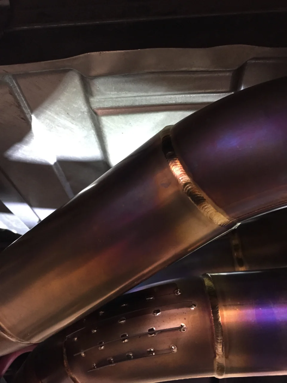 Close-up detail of a custom titanium exhaust system with visible welds and heat discoloration on the piping.