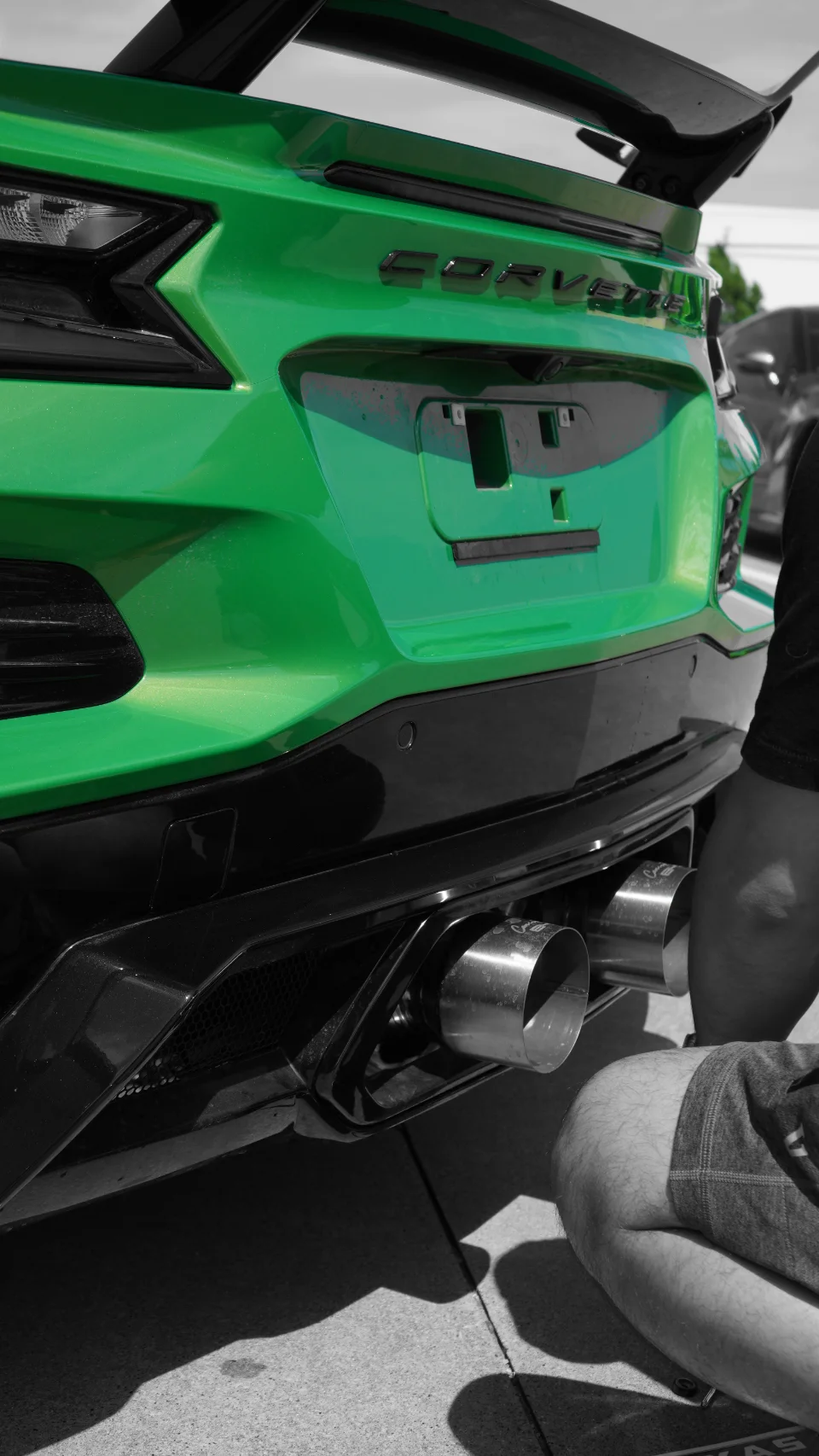 Close-up of the rear of a green C8 Corvette, showing the quad exhaust tips and black diffuser.