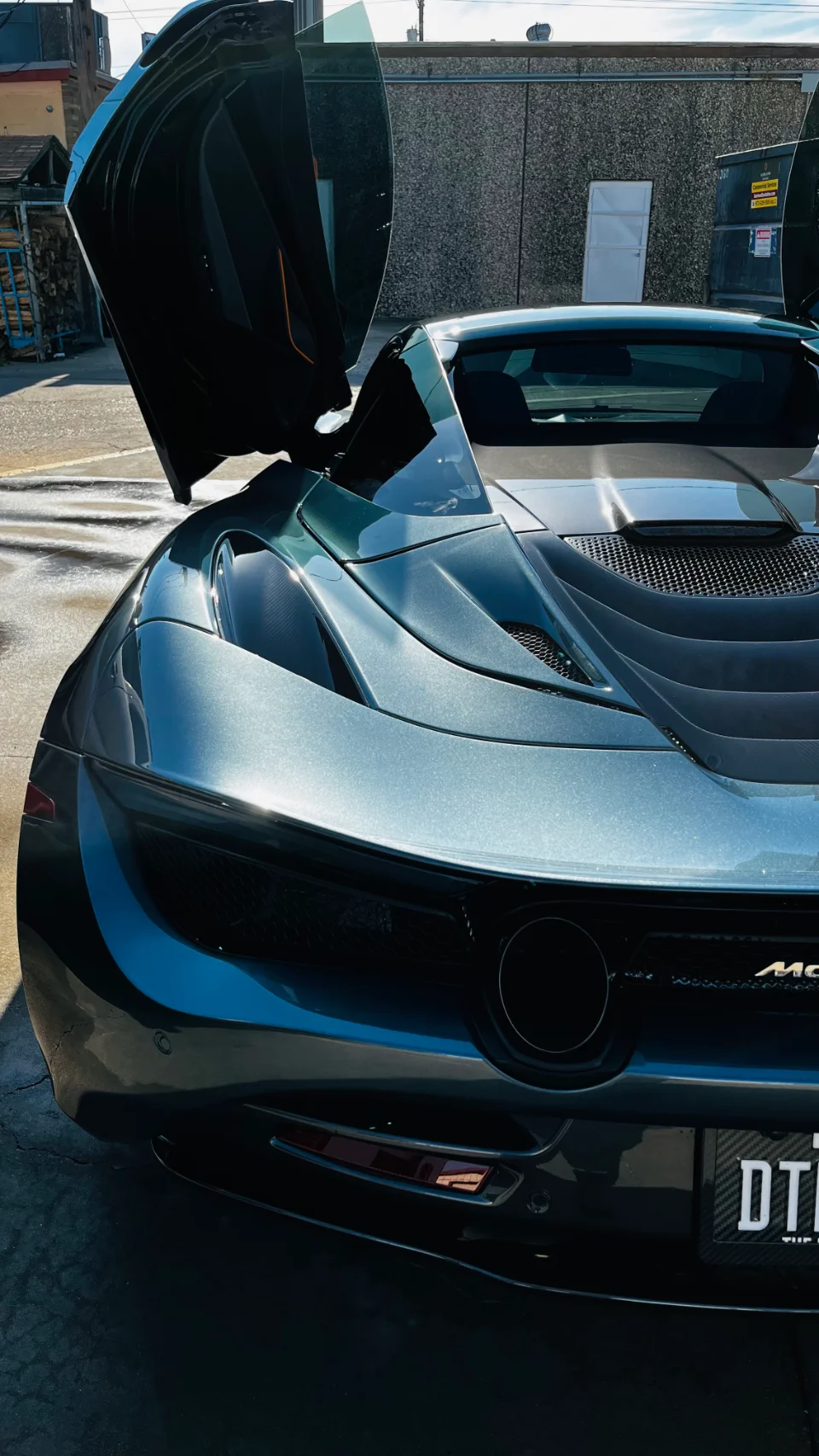 A grey McLaren supercar with its butterfly door open, showcasing its sleek design and rear profile.