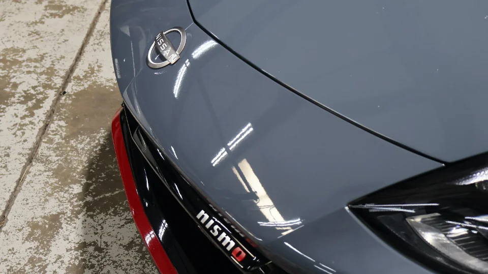 A close-up of the front end of a grey Nissan Z Nismo, showing the Nissan badge and Nismo emblem.