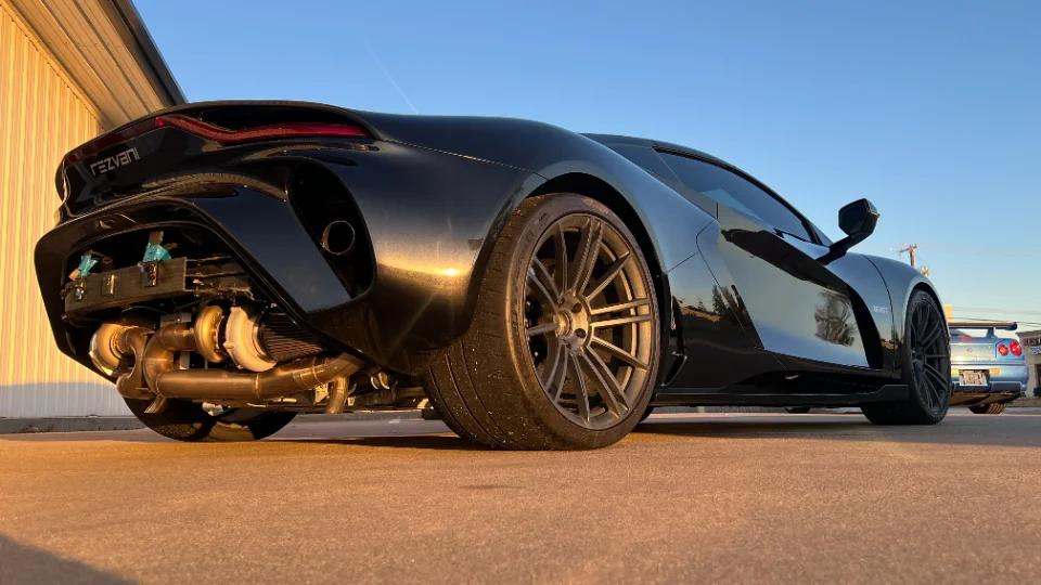 A black Rezvani Beast supercar showcasing its exposed twin-turbo engine and custom exhaust system at sunset.
