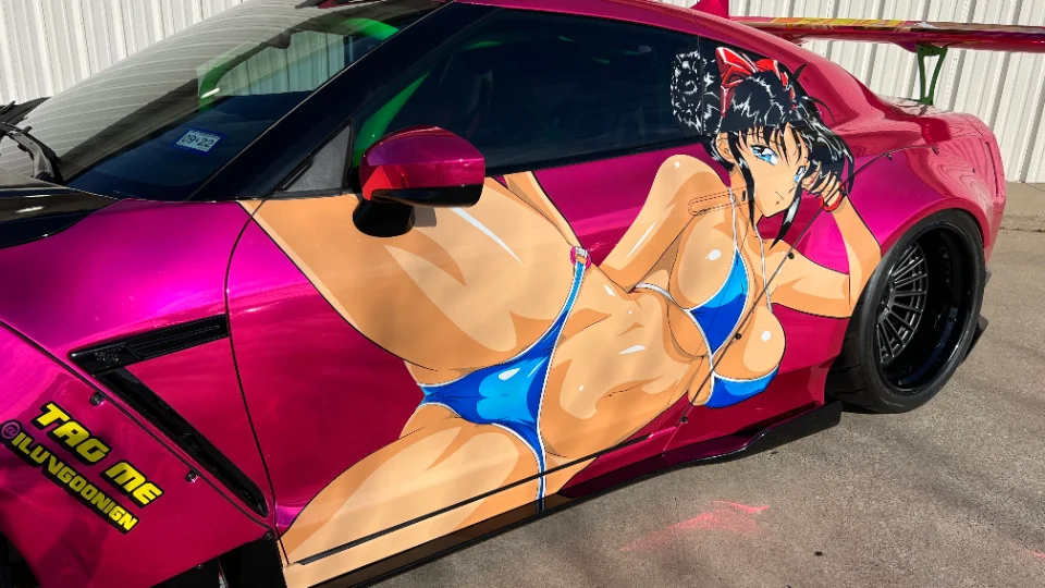 A vibrant pink Nissan GT-R with an anime girl livery, widebody kit, and custom black wheels.