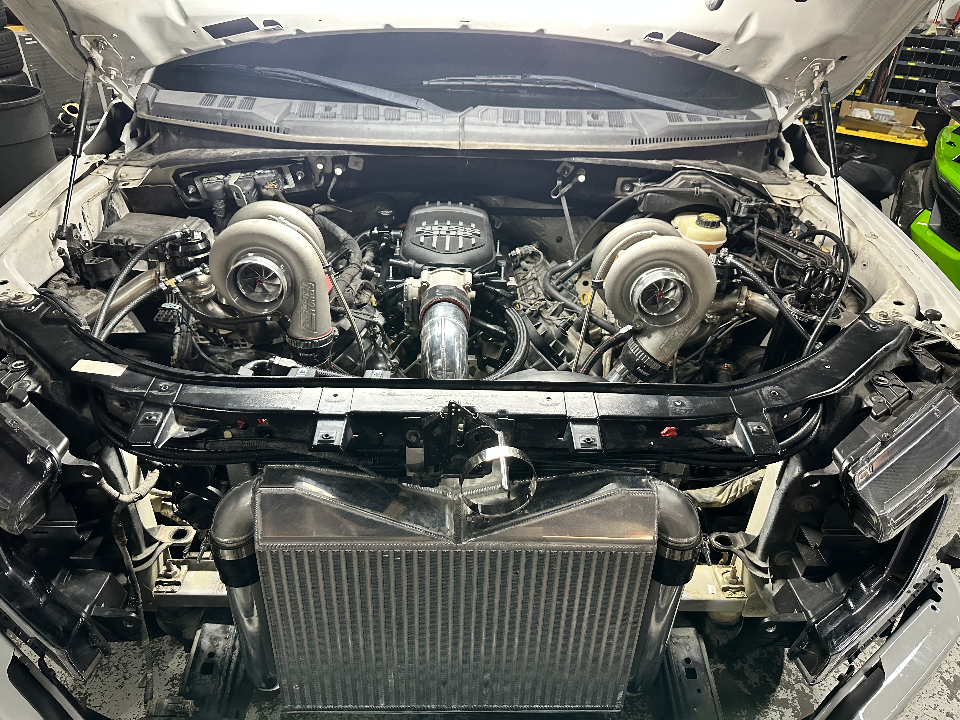 Close-up of a car engine bay with twin turbochargers and a large front-mount intercooler being installed in a performance shop.