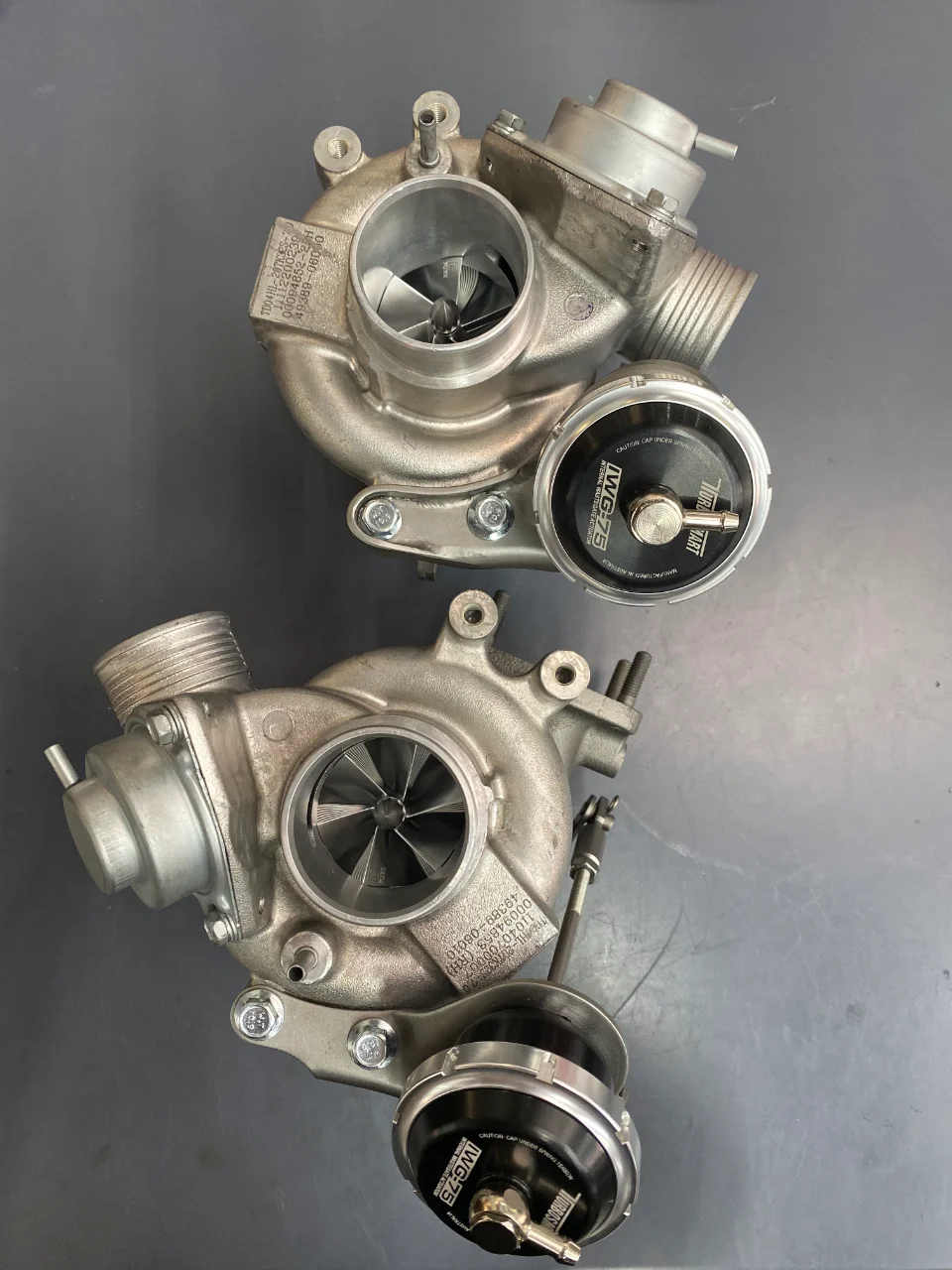 Two performance turbochargers with external wastegates on a grey background, ready for installation.