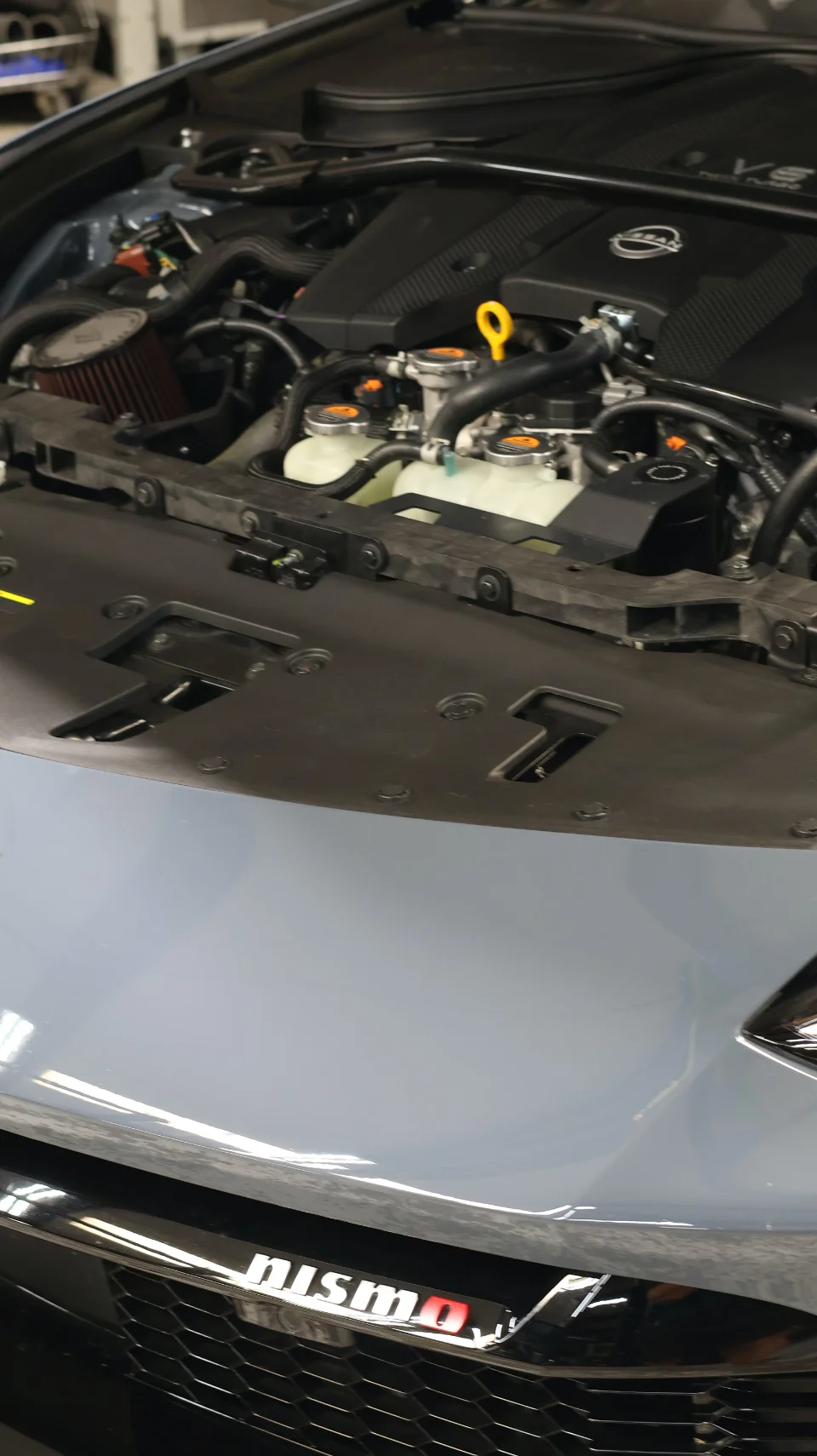 Close-up of a Nissan Z Nismo engine bay with an aftermarket air intake installed, showing the front grille.