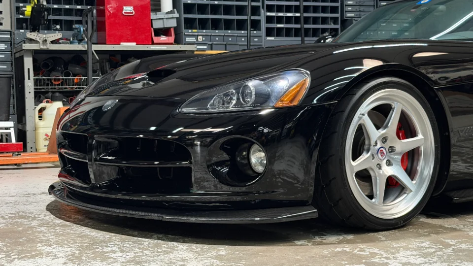 A black Dodge Viper with a carbon fiber front splitter and HRE wheels parked in a performance shop.