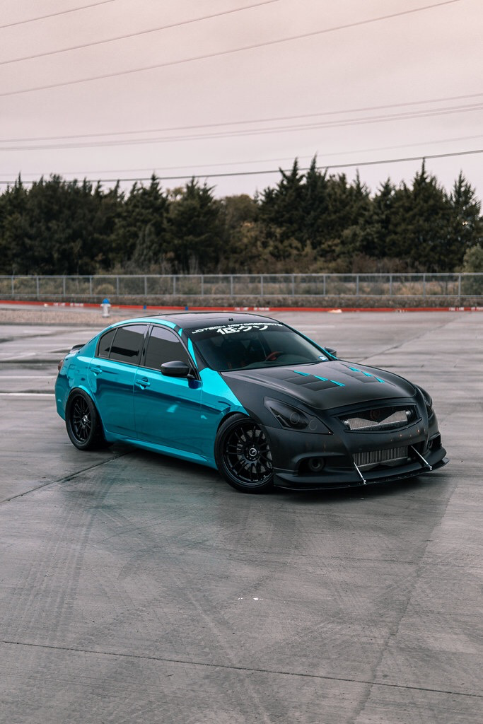 A custom teal and matte black Infiniti G37 sedan with aftermarket wheels and a front splitter parked on an asphalt lot.