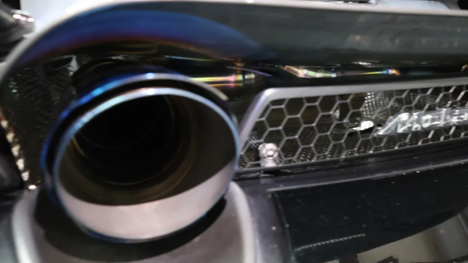 A close-up detail shot of a car's aftermarket titanium exhaust tip with a burnt finish and a honeycomb rear bumper grille.