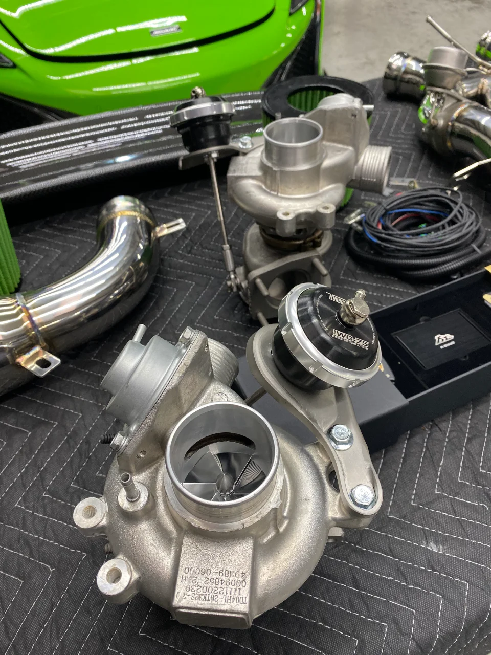 Performance turbochargers, wastegates, and exhaust components laid out in a shop with a green McLaren in the background.