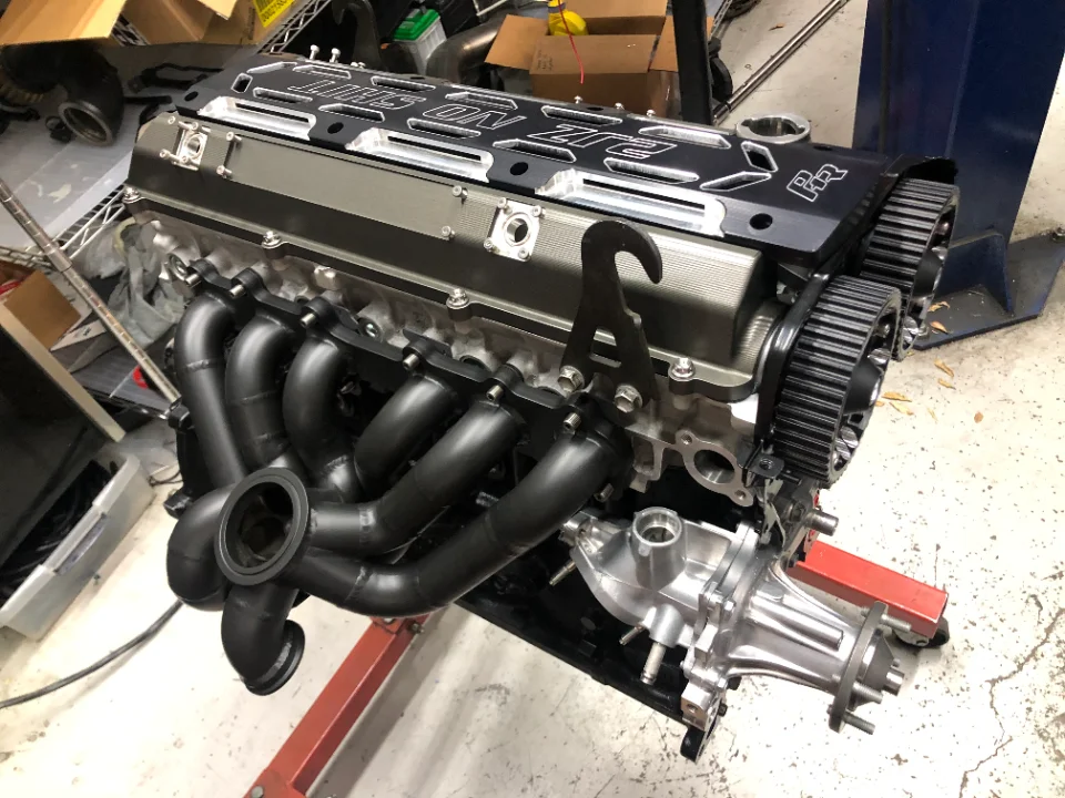 Close-up of a high-performance engine build on an engine stand, featuring a custom valve cover and exhaust manifold.