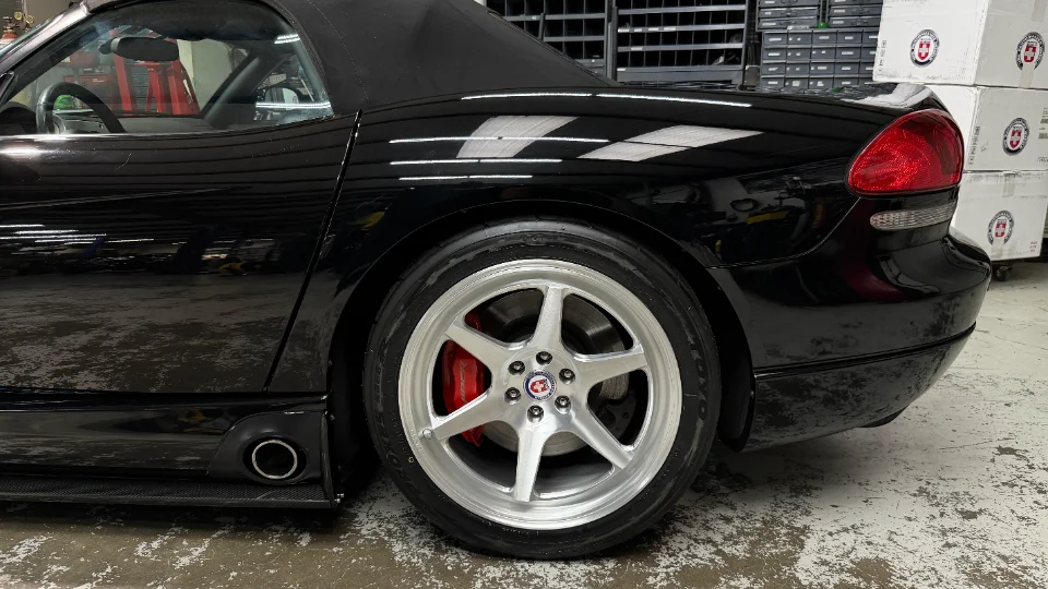 Black Dodge Viper with HRE wheels, red brake calipers, and side exhaust in a clean shop environment.