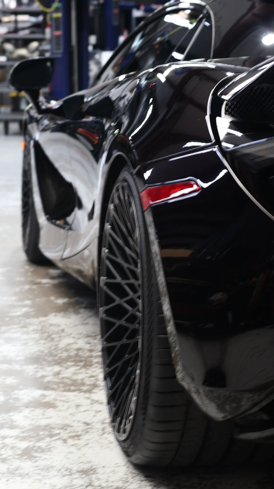 A black McLaren supercar with aftermarket wheels parked in a performance tuning shop.