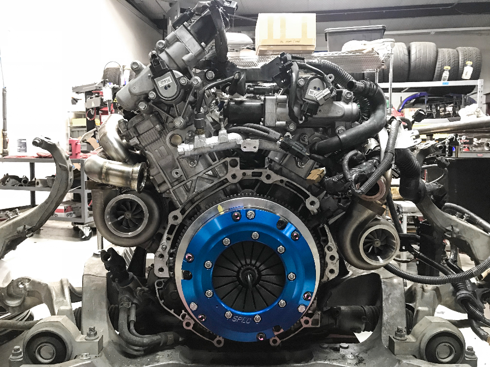 A high-performance engine with twin turbochargers and a blue performance clutch assembly being built in a shop.