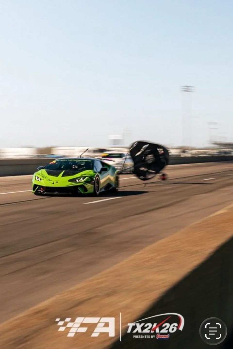 A vibrant green Lamborghini Huracan with a deployed parachute speeds down a drag strip during the TX2K event.