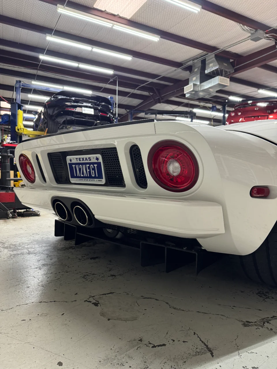 Rear view of a white Ford GT on a lift in a shop, showcasing its aftermarket exhaust and prominent rear diffuser.